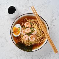 Asian soup with noodles, ramen with shrimps, miso paste, soy sauce. White stone table, top view photo