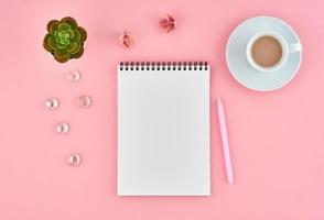 Blank notepad white page and cup of cocoa on pink desk, color background. Top view, flat lay