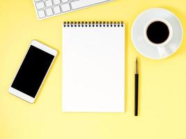 Top view of yellow office desktop with notepad, computer keyboard, smartphone. Mock up, empty space photo