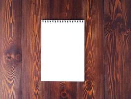 The open notepad with spiral on dark brown wooden table, top view photo