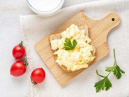 Sandwich with pan-fried scrambled eggs on wooden cutting board, top view. photo
