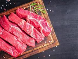 Raw meat, beef steak with seasoning on chopping board on dark background with rosemary, photo