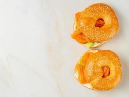 Two sandwiches with salmon, cream cheese, cucumber slices on white marble table, copy space, top view photo