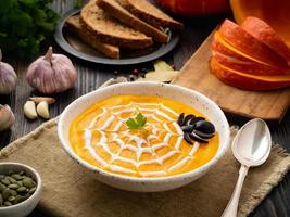 Funny food for Halloween. Pumpkin puree soup, spider web, dark old wooden table, side view. photo
