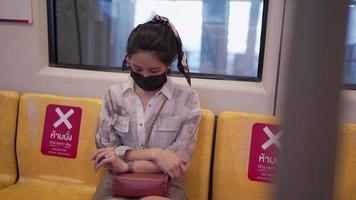 muito jovem mulher asiática usando uma máscara protetora preta sentada no metrô skytrain durante doenças infecciosas covid-19. uma mulher no metrô verifique o relógio do tempo, autoproteção no transporte público. video