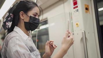 jong aziatisch meisje draagt een zwart masker met behulp van mobiele telefoon als spiegel in de metro, videogesprek met smartphone, forens op de rit covid-19 nieuw normaal, risico op openbaar vervoer, sociale afstand, bangkok thailand