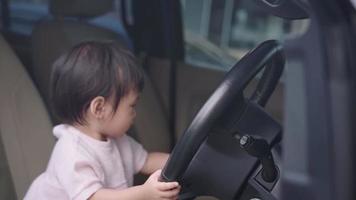 asiatisk liten flicka som leker med bilratten sitter på förarens framsäte, barns nyfikenhet och renhet, glada och glada barn som lär sig färdigheter, oskuldsfulla småbarnsålder kvinna inuti bilen video
