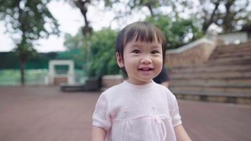 bambino piccolo asiatico che si sente felice sorridente mentre cammina all'interno del parco, membro più giovane della famiglia, bambino che fa il primo passo, inizio di una nuova vita, innocenza bambina impara a camminare, bambino gioioso video