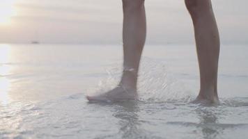 sidovy ung kvinna ben och fötter som går längs havsvattenvågor på stranden, under gyllene solnedgångstimme, lugn slappna av lugnt tänkande kontemplation, öparadis reträtt, låg vinkelbild video