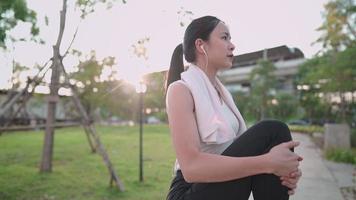 Mujer joven en forma asiática estirando las piernas de pie, sosteniendo las piernas con ambas manos, enfriándose después del ejercicio, músculos y articulaciones flexibles, campo de hierba verde en el fondo, prevención de lesiones, en forma y firme video