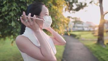 mujer joven asiática quita la máscara facial prepárate para correr en el parque al aire libre, al atardecer, ambiente fresco y relajado, estilo de vida de mujer soltera, condición médica de salud, emoción positiva mujer alegre video