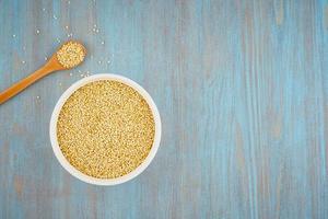 quinoa seed grain in white bowl and spoon on blue table, copy space photo