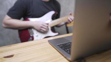 close-up van een wazige jonge rockman die elektrische gitaar oefent achter digitale laptop, online recreatieve technologie, een gitarist die nieuwe akkoorden leert in een modern huis, muzikant die tekst maakt video