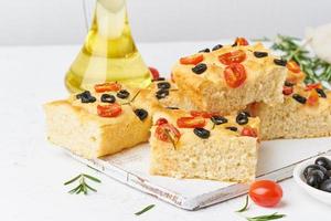 Sliced pieces of focaccia with tomatoes, olives and rosemary. Traditional Italian flat bread. photo