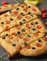 Focaccia, pizza, italian flat bread with tomatoes, olives and rosemary on dark brown table photo