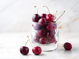 red dark sweet cherries in glass on stone white table, side view, copy space