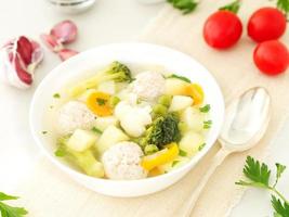 bowl of soup, a cup of broth and vegetables, meatballs made of turkey and chicken, side view