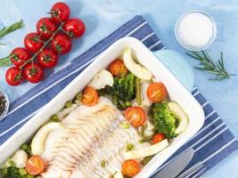 Fish cod baked in blue oven with vegetables - broccoli, tomatoes. Healthy diet food. Blue stone background, top view. photo