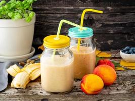 banana peach nectarine smoothie in two jars, fresh fruit milkshakes on old dark rustic wooden table, side view photo