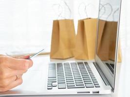 mujer sentada en la mesa, mirando la computadora portátil, pagando las compras con tarjeta de crédito, compras en línea foto