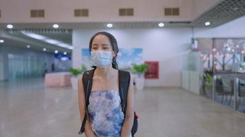 Asian Young female wear medical protective face mask walking with backpack inside airport terminal, infectious diseases prevention, departure arrival waving hand greeting family, new normal pandemic