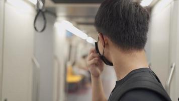 aziatische jonge man die in de metro in de luchttrein staat, aan de telefoon praat tijdens covid-19 pandemie, nieuw normaal concept voor openbaar vervoer, sociale afstand, risico op infectieziekte
