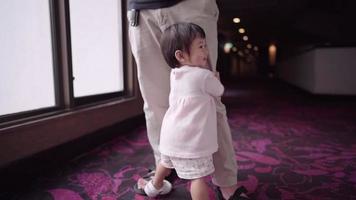 Asiatisches glückliches kleines Mädchen, das die Beine ihres Vaters hält, herumspielt, ungezogenes und sorgloses Kind, Familienwärme, Kleinkinder-Schritte beim ersten Schritt üben, Kinderlernfähigkeiten, verspielte Tochter video