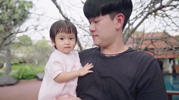 família se reunindo dentro do parque, jovem pai asiático segurando sua filhinha nos braços, calor da família passando tempo juntos no parque, desenvolvimento infantil de tenra idade, cuidado de amor video