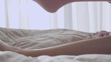 close-up nas pernas da mulher acorda, sente-se usando meias cor de rosa na cama, cortina branca de luz solar da manhã quente, confortável cobertor de lençóis de quarto aconchegante, temperatura do corpo mantenha-se aquecido, coloque meias