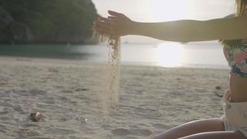Young fit woman hands playing with sand on beach during a day, handful of soft fine white sand, pouring sand, carefree girl on summer holiday vacation, sit down on tropical beach island, slow motion