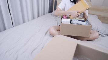 Asian young female open parcel delivery box, sit down inside bedroom, moving in new house, new apartment, Sorting cleaning house, Relocating concept, hobbies lifestyles, charity donation preparation