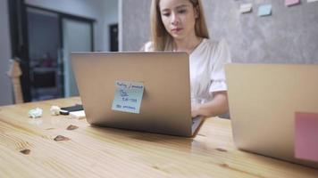 asiatische blonde Büroangestellte, die einen Laptop verwendet, um Geschäftsinformationen zu sammeln, konzentriert auf den Bildschirm starrt, auf der Tastatur tippt, spät im Büro arbeitet, erfolgreiche, engagierte Mitarbeiter