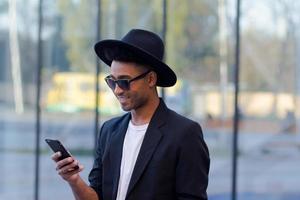 joven hombre feliz con traje negro y sombrero negro, concepto de hombre de negocios moderno foto