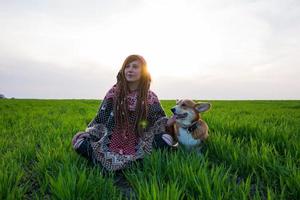 mujer joven en poncho con perro corgi relajándose en los campos de primavera foto