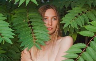 retrato de una bella joven con hojas verdes, una bella dama rubia con arbustos de primavera foto