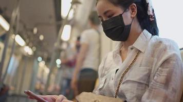 mujeres asiáticas con máscara protectora negra sentadas en el metro usando un teléfono inteligente. viaje a casa durante covid-19 nueva normalidad, mujer en metro, autoprotección en transporte público, concepto de distanciamiento social