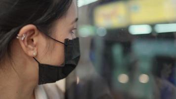 aziatische vrouw draagt een zwart masker en kijkt naar buiten met reflectie, staande naast de treindeur. covid-19 pandemische ziekte, openbaar vervoer, na vermoeiende dag op het werk, nieuw normaal, verdrietig en hopeloos