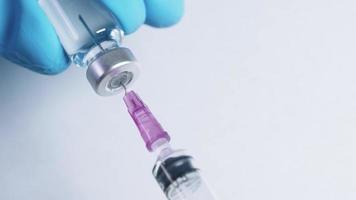 Extreme close up a hypodermic needle in a vaccine bottle sucking transparent liquid slowly into syringe, professional nurse with medical glove on hand holding a medical serum for injecting medical video