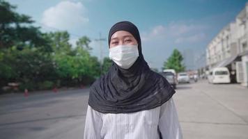 la giovane donna musulmana asiatica indossa una maschera protettiva che cammina lungo la strada pedonale urbana sul lato della strada, nuovo normale blocco pandemico, rischio di infezioni, prevenzione dal virus, diritti positivi della donna, giornata di sole video