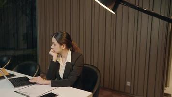 une femme d'affaires travailleuse en costume de travail formel fait des heures supplémentaires jusqu'à tard dans la nuit seule avec un ordinateur portable et des papiers au bureau, gestion de l'analyse des données, jeune entrepreneur pense planificateur video