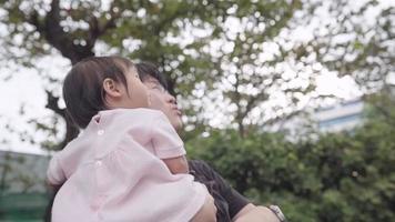 jovem pai asiático e sua adorável bebê infantil olhando para o céu dentro do parque em pé debaixo de árvores, vínculo de cuidados infantis, curiosidade de inocência de crianças, pai e filha