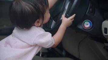 asiatisches weibliches kind, das sich wundert, im auto zu spielen, lernfähigkeiten für die entwicklung von kindern, fahrzeug, das mit dem lenkrad spielt, baby, das auf dem autofahrersitz sitzt, glückliches mädchen, das vorgibt, ein fahrer zu sein