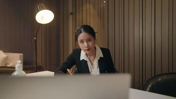 Fokussierte asiatische Geschäftsfrau, die im Büro am Schreibtisch mit Computer-Notebook arbeitet. weibliche berufstätige schreiben ernsthaft wichtige informationen auf. Geschäftsfrau mit Laptop und starrt auf den Bildschirm