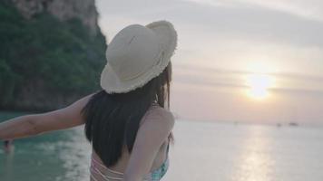 en ung kvinna med svart hår som höjer armarna och sträcker ut kroppen efter att ha solat på kvällen, avkopplande fritidsaktivitet, sommarstrandsemesterresa, tropisk havsbild med en grön bergsutsikt bakom video