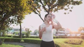 mujer joven asiática corriendo en el parque, usando una toalla limpiando el sudor de la cara, durante el seguro de atención médica nutricional de la dieta de la puesta del sol, auto motivación chica dura corre con una hermosa puesta de sol en el fondo video