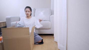 shot of young putting things into the parcel carton box, preparing to move out, sit down couch on the background, Multitasking works house arranging, budget Relocating financial crisis, stay at home video