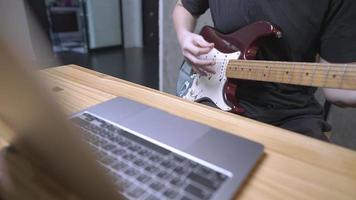 Playing guitar writing composing songs using laptop mobile recording music singing live stream social media entertaining people, working at home in living room,  internet vlog website or influencer video