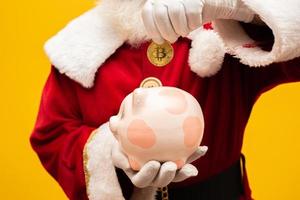 Santa Claus putting coin into a ceramic piggy bank. Savings concept for the end of the year. Spending over Christmas. Spent on Christmas presents. photo