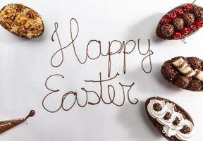 Happy Easter written with melted chocolate on white background. With gourmet Easter eggs decorating on the sides. photo