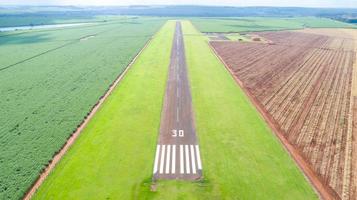 vista aérea de la pista de aterrizaje pavimentada del avión en brasil. pequeños aviones de hélice pista de aterrizaje remota con plantaciones de caña de azúcar en el fondo. foto